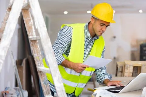 Man engineer checking documents and using laptop during repair works Stock Photos