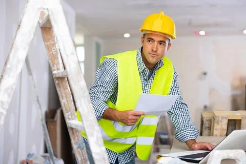 Man engineer checking documents and using laptop during repair works Stock Photos