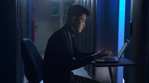 Man engineer checking hardware racks and working with laptop, sitting at table Stock Footage 164910642