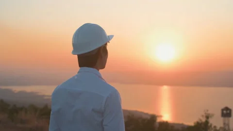A man engineer is putting a protective helmet on his head at sunset. Stock Footage 149001273