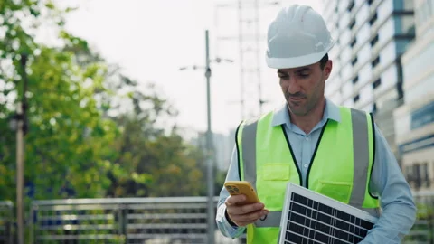 Man engineer reads message on smartphone holding solar panel walking against Video stock 296874832