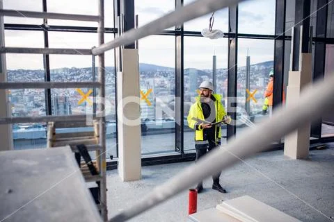 Man engineer standing on construction site, holding blueprints. Stock Photos