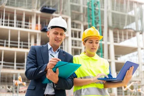 Man engineer standing on a construction site with a young woman worker monitors Stock Photos