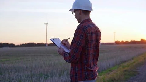 Man engineer wearing a white protective helmet is taking notes with a clipboard Stock-Fotos