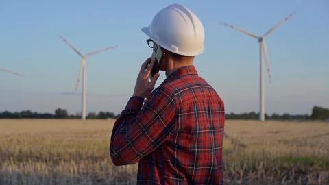 Man engineer, wearing a white protective helmet is talking by smartphone in a Foto stock