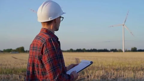 Man engineer, wearing a white protective helmet is taking notes with a clipboard Stock Photos