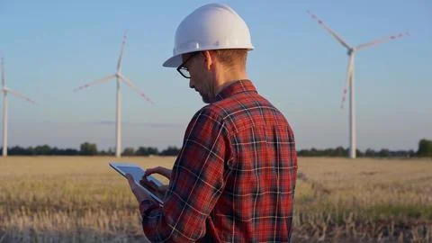 Man engineer at work is taking notes with a tablet computer in a field with wind Stock-Fotos