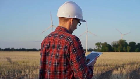 Man engineer at work is taking notes with a tablet computer in a field with wind Stock Photos