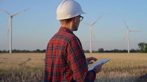 Man engineer at work is wearing a white protective helmet and taking notes with Stock Photos