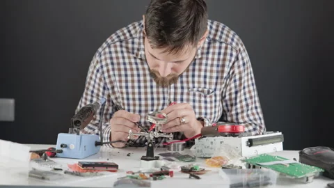A man with engineering skills checks the circuit board with a multimeter Stock Footage 265561285