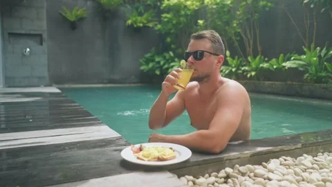 Man enjoying breakfast while relaxing in private swimming pool Stock Footage 340847870