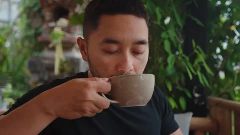 Man enjoying coffee while relaxing at a tropical cafe in Ubud, Bali. Stockbeeldmateriaal 347795824