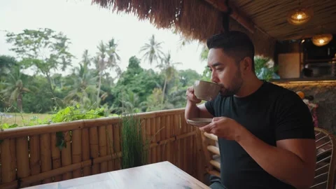 Man enjoying coffee while relaxing at a tropical cafe in Ubud, Bali. Vidéo 347802132