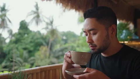 Man enjoying coffee while relaxing at a tropical cafe in Ubud, Bali. Видео 347806891