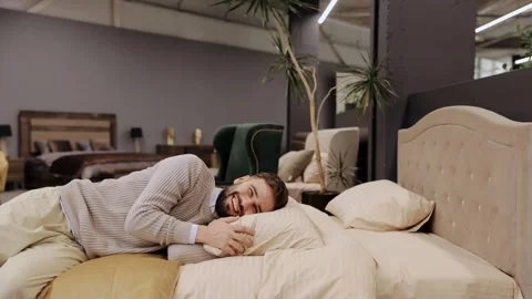 Man enjoying comfort lying on bed in furniture store Stock Footage 322550168
