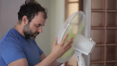 Man Enjoying Cool Wind From Electric Fan at Home at Summer Day. Male Suffer.. Видео 303921182