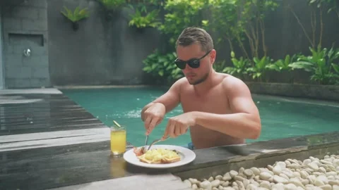 Man enjoying floating breakfast in swimming pool on vacation 库存影片 340847819