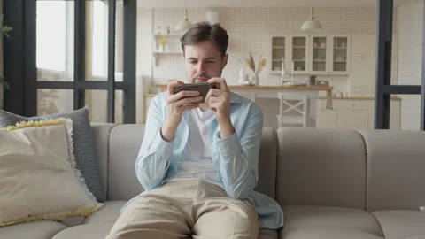 Man Enjoying Mobile Game On Sofa In Bright Modern Living Room Interior Stock Footage 304581673