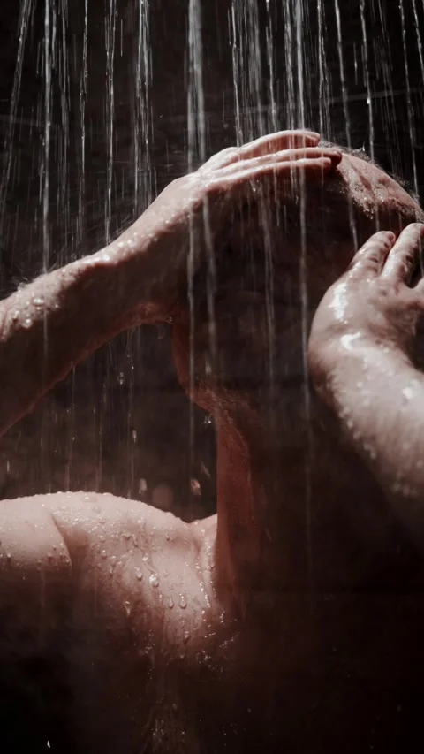 Man enjoying a refreshing shower in a dimly lit space while water cascades down Stock Footage 312864187