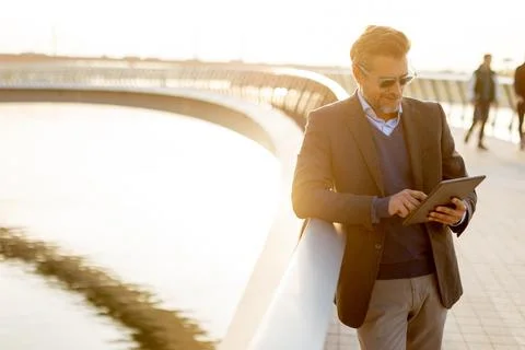 Man enjoying sunset by the river while holding a tablet and smiling in a be.. Foto stock