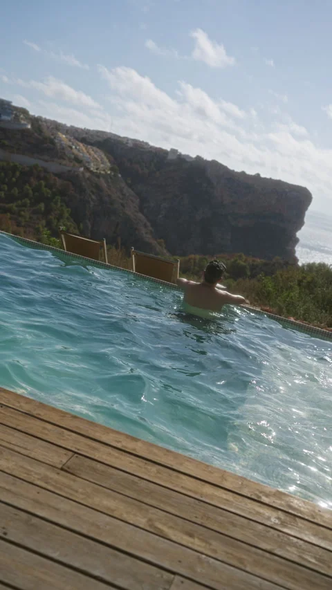 Man enjoying a swim in an infinity pool with stunning cliffside and ocean v.. Stock Footage 285740457