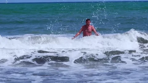 A man enjoying the waves on the beach, experiencing joy under a sunny summer sky Stockbeeldmateriaal 276646341