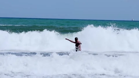 A man enjoying the waves on the beach, experiencing joy under a sunny summer sky Stock Footage 276646346