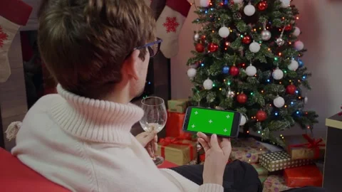 Man enjoying wine and scrolling Green Screen Mockup phone in a Christmas Stock-Footage 314781140
