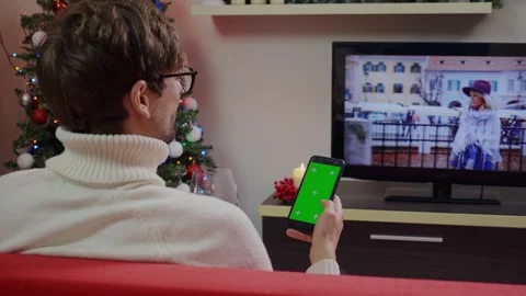 Man enjoying wine and scrolling Green Screen Mockup phone in a Christmas Stock-Footage 314781908
