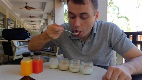 Man enjoying yogurt with spoon at table, sharing fruit juice and tasty cuisine Stock Footage 264964735