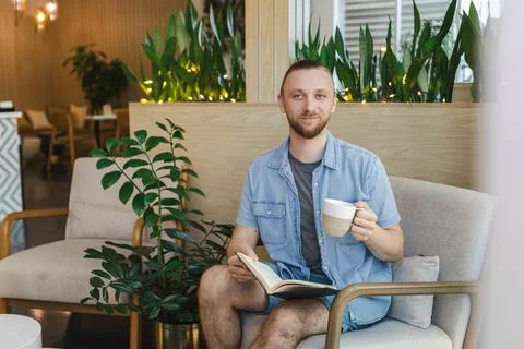 Man enjoys a book while drinking coffee in a modern cafe setting during a r.. 写真素材