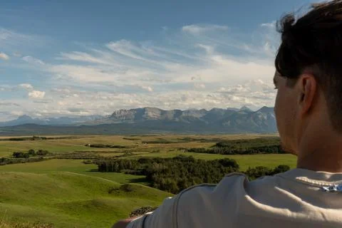 A man enjoys a mountain view, clear blue sky, with green rolling hills. Stock Photos