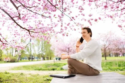 A man enjoys remote work and freelancing outdoors in a park, talking on the.. Foto stock