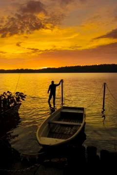 Man enjoys sunset while untying boat at Lake Stock Photos