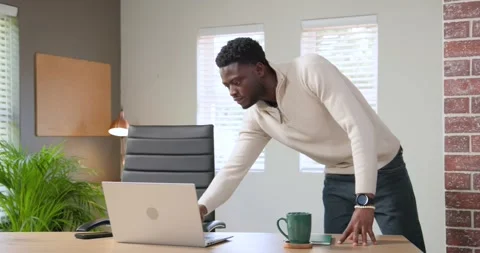 Man entering office, adjusting laptop at desk while steadying green mug and Stock Footage 343888906