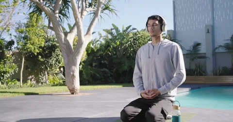 Man entering poolside, putting on headphones, kneeling on mat by pool, Stock Footage 342084615