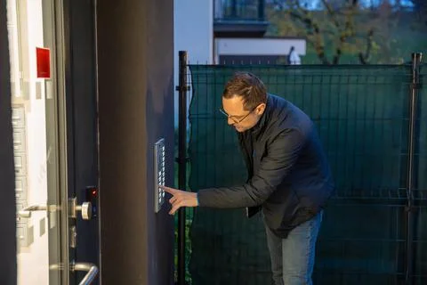 Man entering security code on a door panel outside residential building. Evening Stock Photos