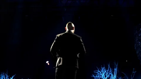 Man entertainer, presenter or actor on stage. Back, arms to sides, smoke on Stock Footage 121726350