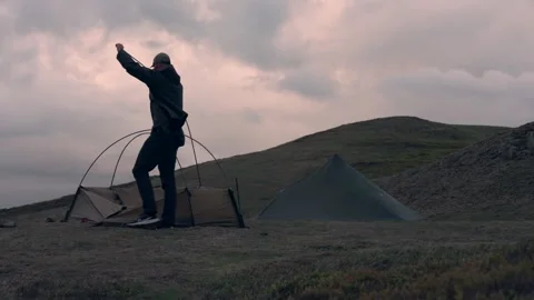 A man erecting a tent on a hill beside another while camping Stock Footage 346638798