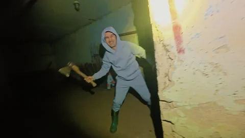 A man escapes from a psycho with an axe, running away through a dark basement. Video stock 331149599