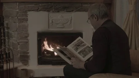 A man in the evening examines a book in front of a fireplace Stock Footage 74244885