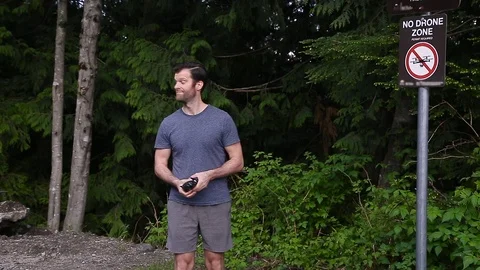 A man in an evergreen forest holding a small drone gets ready to fly until he Stock Footage 108884470