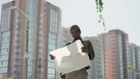 Man Examines Crumpled Map Against Urban High Rise Background showing paper Stock Footage 345127514