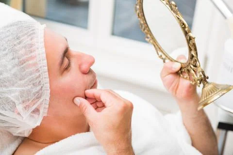 Man examines face in mirror lying in beauty salon Stock Photos