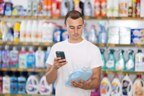 Man examines liquid laundry detergent in supermarket department and scans QR Stock Photos