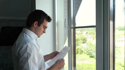 Man examines papers while standing by the window Stock Footage 158896295