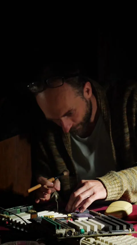Man Examining Circuit Board in a Dimly Lit Workspace Stock Footage 292917233