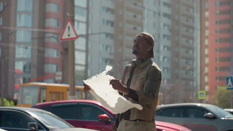 Man Examining Crumpled Paper Map in Urban Street Scene with Tall Buildings and Stock Footage 345840025