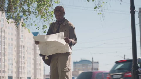 Man examining large paper map on busy city street with cars and tall buildings Stock Footage 345125506