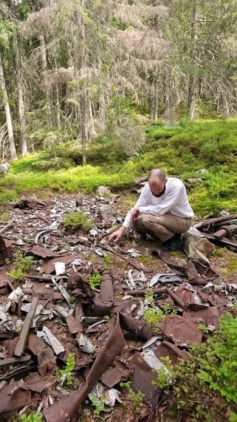 Man examining rusted plane crash wreckage on mountain forest slope Stock Footage 344877421